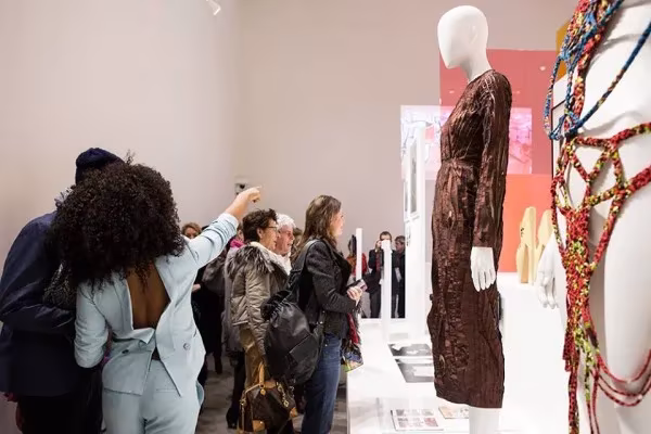 Visitantes ante un maniquí con vestido marrón y piezas de abalorios en la exposición «Making Africa»