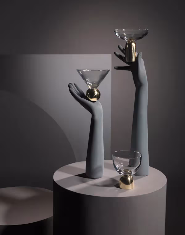 Copas de cristal sostenidas por manos escultóricas grises en la instalación de Lee Broom