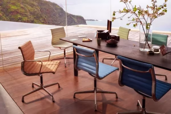 Sillas Aluminium de Eames en varios colores alrededor de una mesa larga en una terraza junto al mar