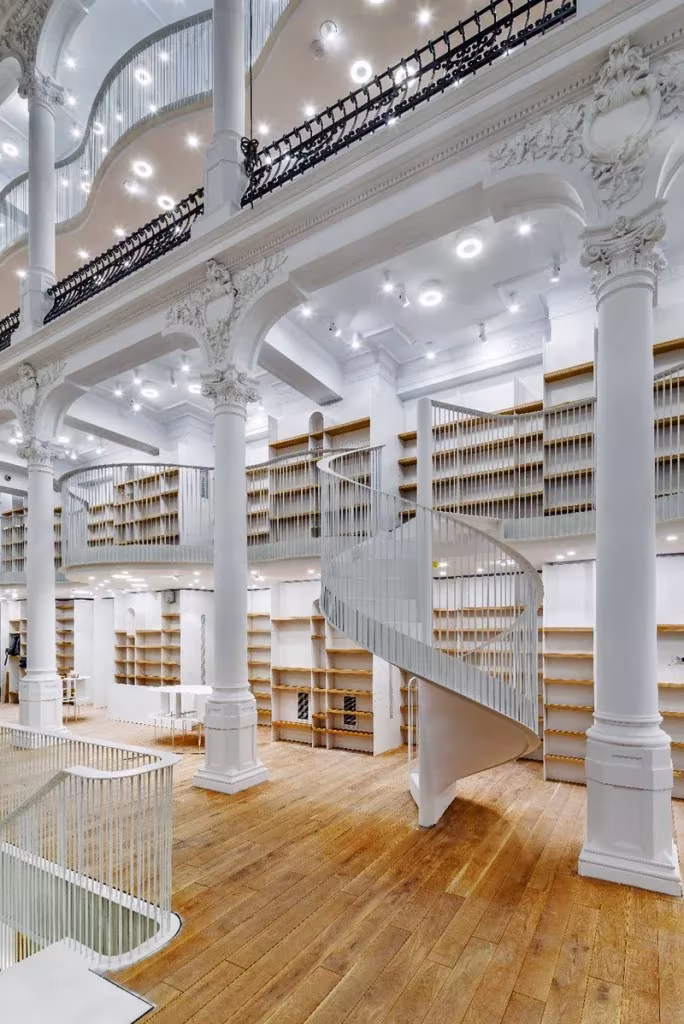 Escalera de caracol blanca entre columnas de hierro y estanterías de madera en Carturesti Carusel
