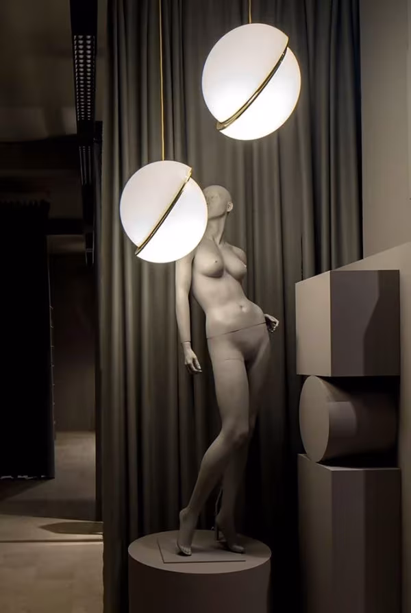 Lámparas Crescent de Lee Broom junto a un maniquí blanco ante cortinas oscuras en «The Department Store»