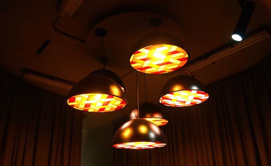 Lámparas colgantes de Lee Broom con pantallas tejidas en rojo y amarillo iluminadas en la penumbra