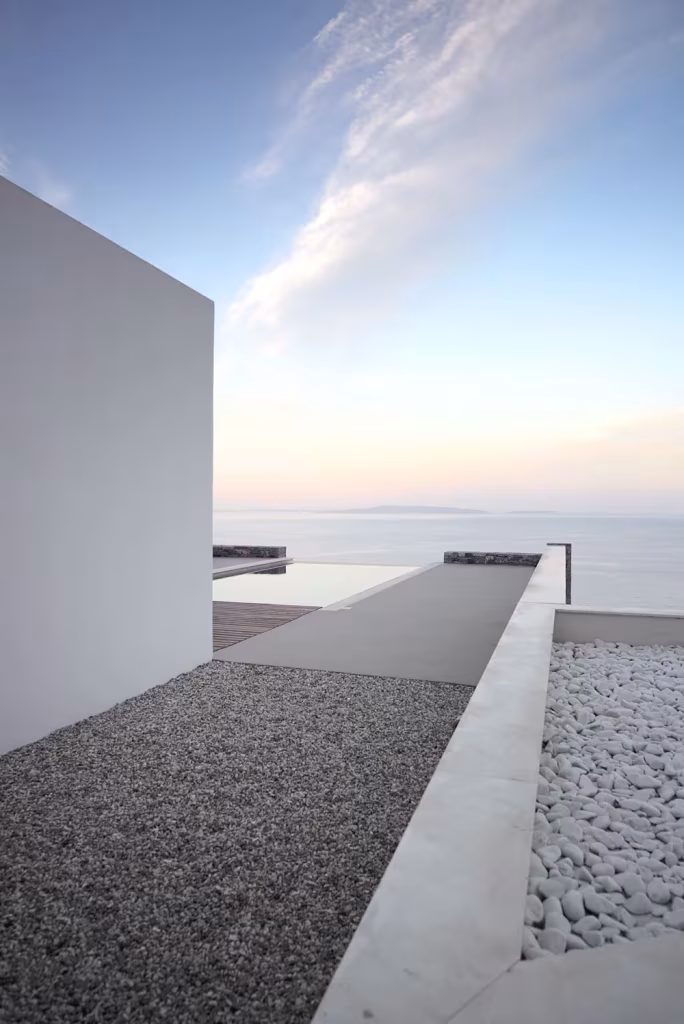 Pasillo exterior de grava entre un muro blanco y el horizonte del mar en Villa Melana