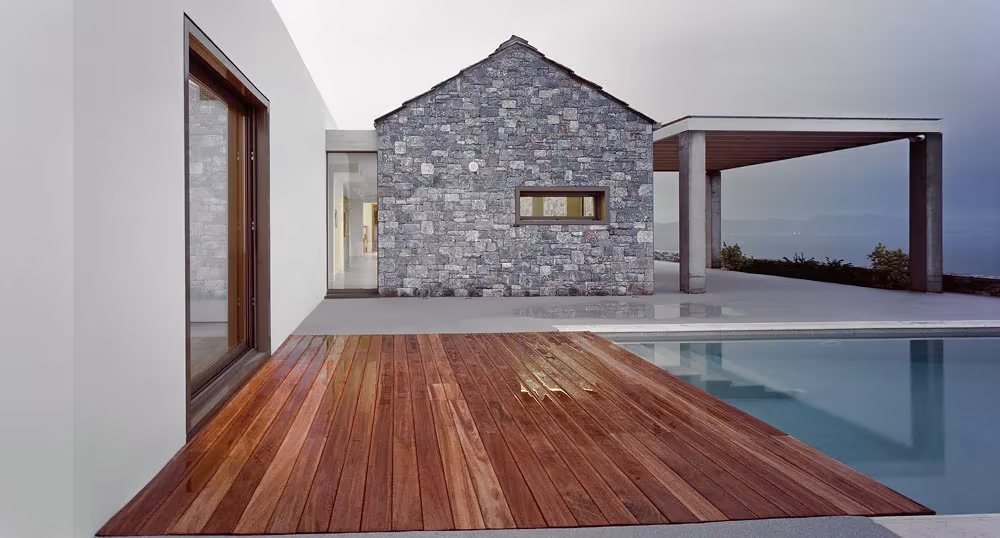Tarima de madera junto a la piscina frente a la casita de piedra a dos aguas de Villa Melana