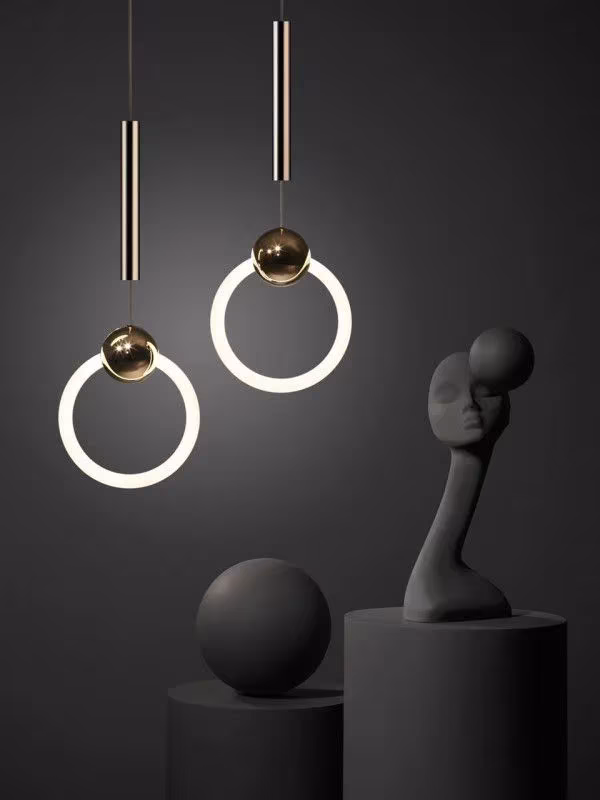Lámparas colgantes de anillo luminoso de Lee Broom junto a esculturas negras sobre fondo oscuro