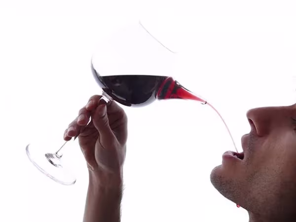 Copa de vino con pico vertedor por la que una persona bebe un chorro de vino tinto
