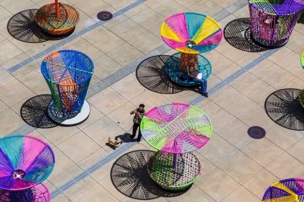 Vista aérea de Los Trompos de colores sobre una plaza pavimentada, con personas entre ellos