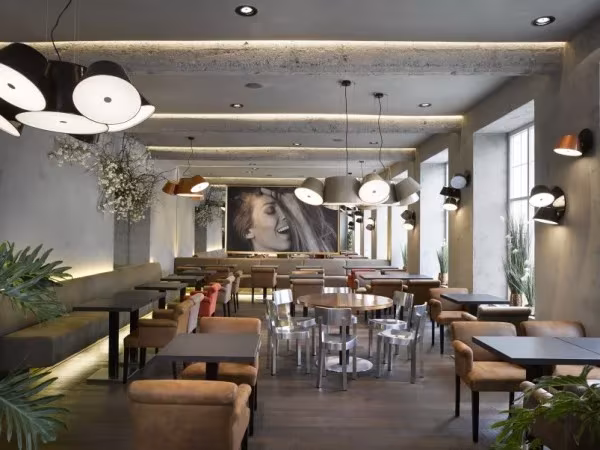 Cafetería alargada con mesas, plantas y lámparas Marset de pantallas negras agrupadas