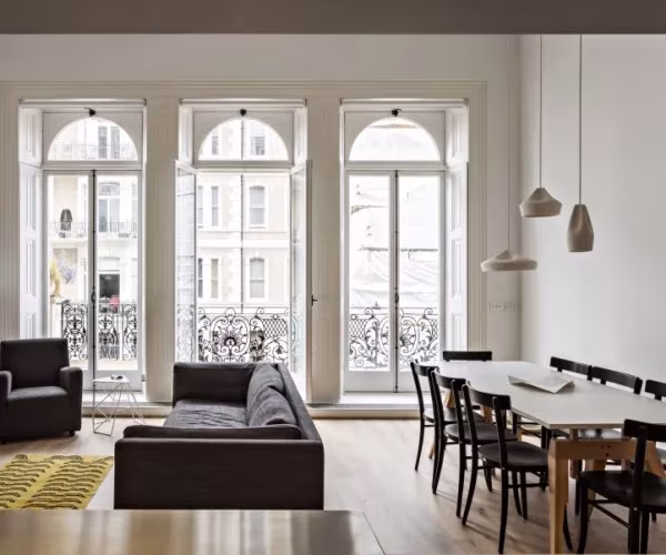 Piso en Londres con sofá gris, mesa de comedor y lámparas colgantes Marset junto a ventanales en arco