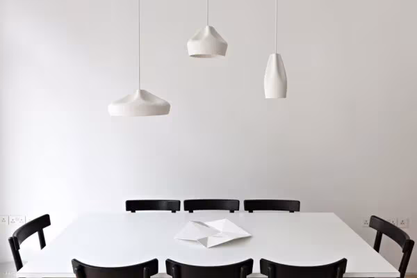 Comedor blanco con mesa, sillas negras y tres lámparas colgantes de cerámica de Marset