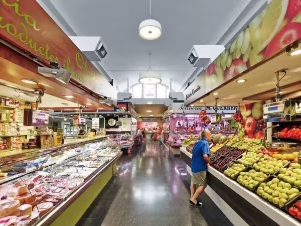 Mercat de la Guineueta con puestos de fruta y charcutería iluminados por lámparas de Marset