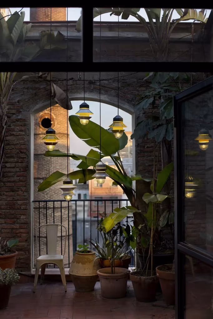 Lámparas Santorini colgadas en un patio de ladrillo con plantas tropicales y macetas de barro