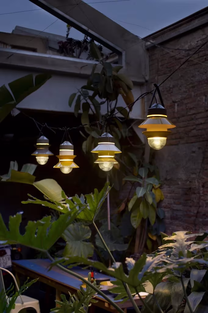 Guirnalda Santorini de Marset encendida entre hojas grandes en una terraza al anochecer