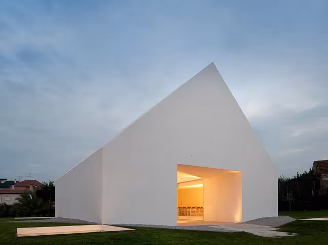 Casa Leiria, volumen blanco a dos aguas con una abertura iluminada en la base sobre el césped