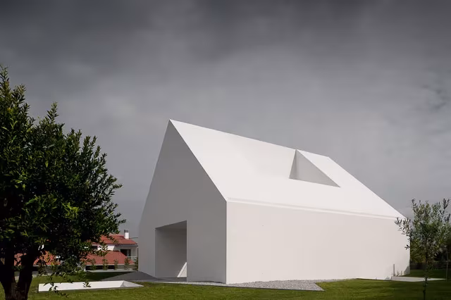 Volumen blanco de la Casa Leiria con hueco en la cubierta bajo un cielo gris y un árbol al lado