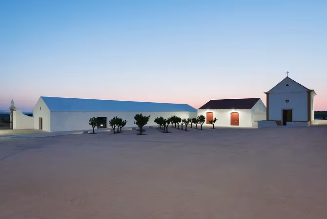 Explanada del Hotel Torre de Palma al atardecer, con nave blanca, hilera de olivos y una pequeña capilla encalada