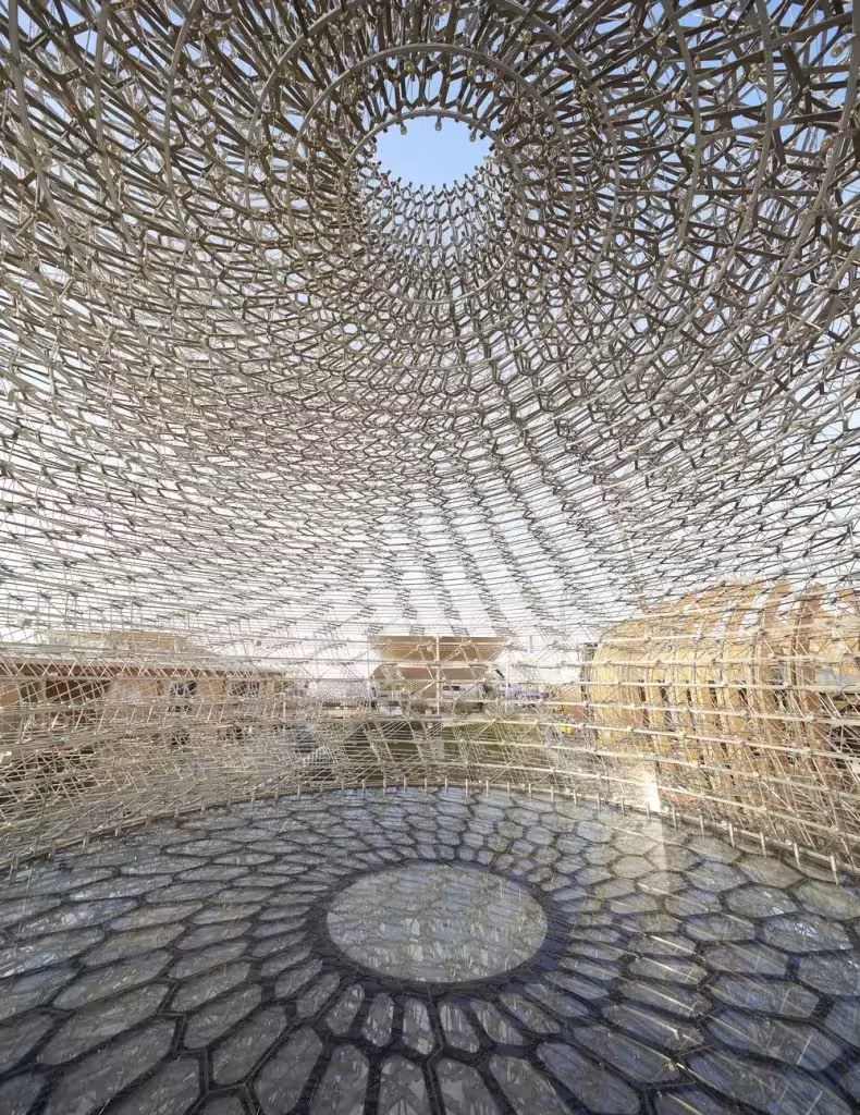 Interior de La Colmena con suelo de vidrio hexagonal y bóveda de varillas metálicas abierta en un óculo central