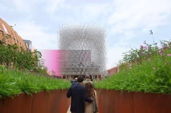 Pareja paseando entre parterres de flores silvestres hacia La Colmena, pabellón de Reino Unido en la Expo de Milán