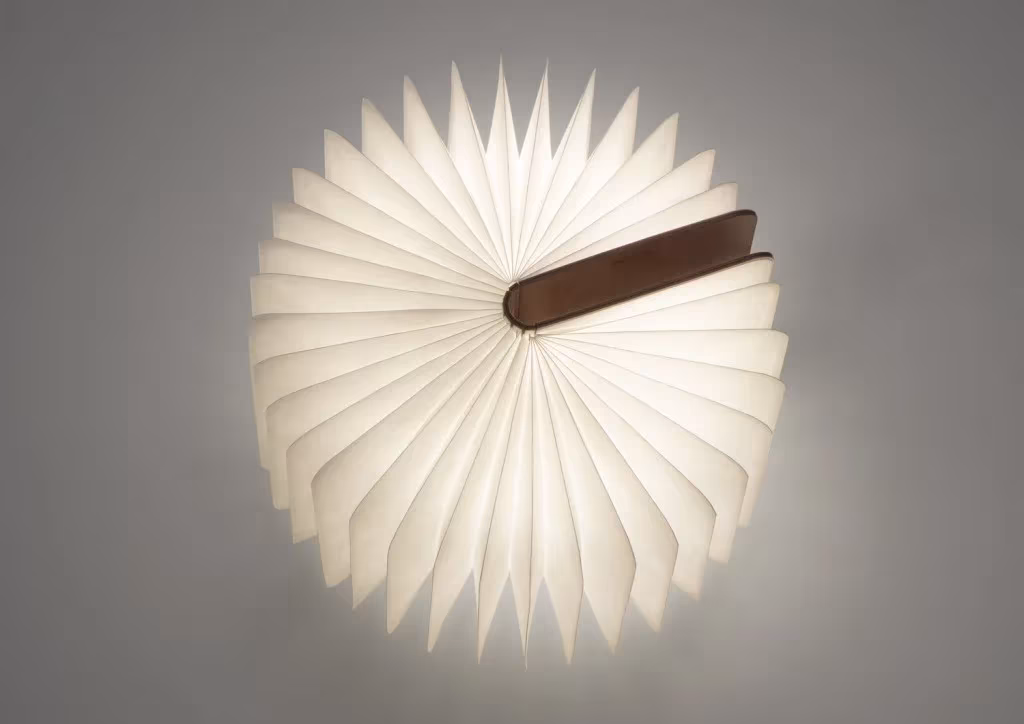 Lámpara Lumio abierta en círculo completo como un abanico de papel iluminado, con tapas de madera oscura