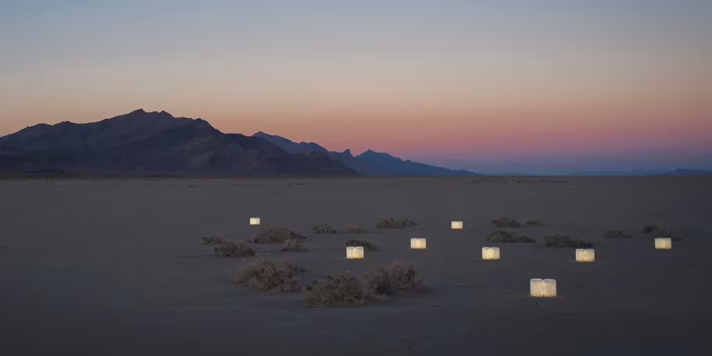 Varias lámparas Lumio encendidas sobre un desierto al anochecer con montañas en el horizonte