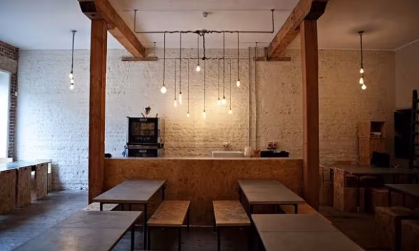 Comedor del restaurante Silo con vigas de madera, bombillas colgantes, mesas largas y pared de ladrillo blanco