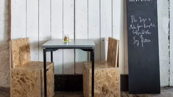 Mesa para dos con sillas de tablero OSB y pizarra con menú escrito a tiza en el restaurante Silo