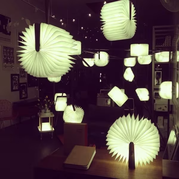 Decenas de lámparas Lumio abiertas en distintas formas iluminando un espacio oscuro con luz verdosa
