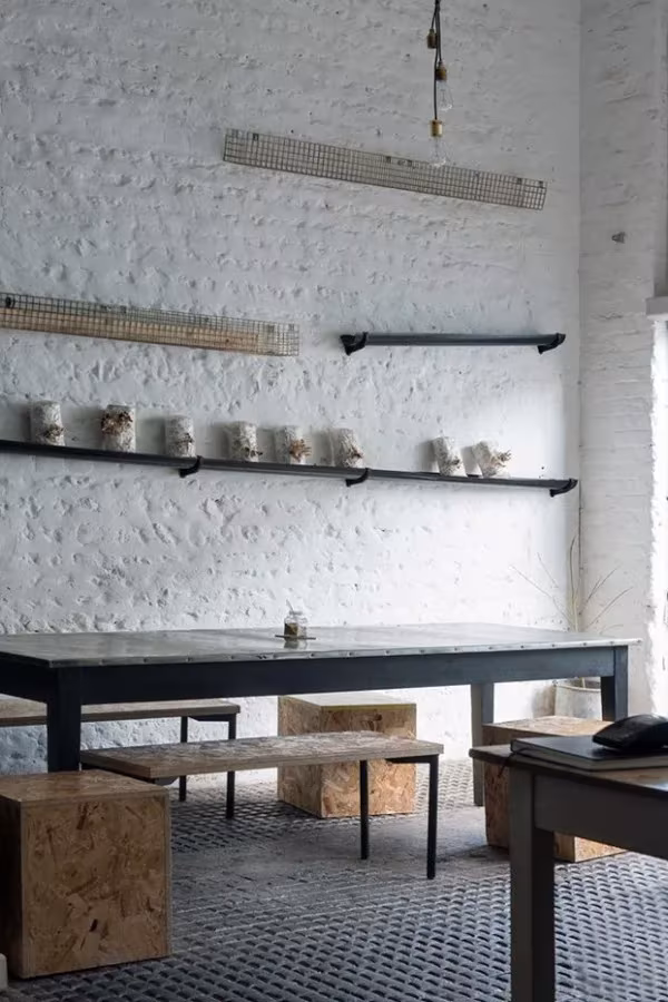 Comedor del restaurante Silo con pared de ladrillo blanco, baldas negras con tarros y mesa larga con bancos de aglomerado