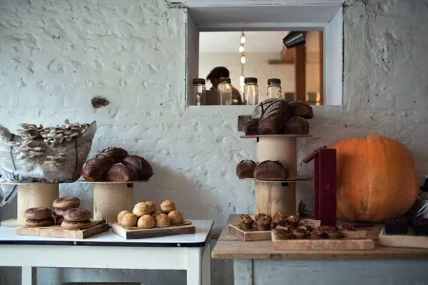 Mostrador del restaurante Silo con panes y bollos expuestos, una calabaza y ventanuco a la cocina en pared encalada