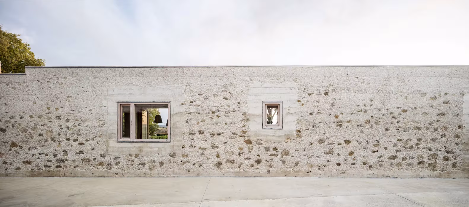 Muro de piedra con dos pequeñas ventanas de madera en la fachada de la Casa 1413 de H Arquitectes, Ullastret