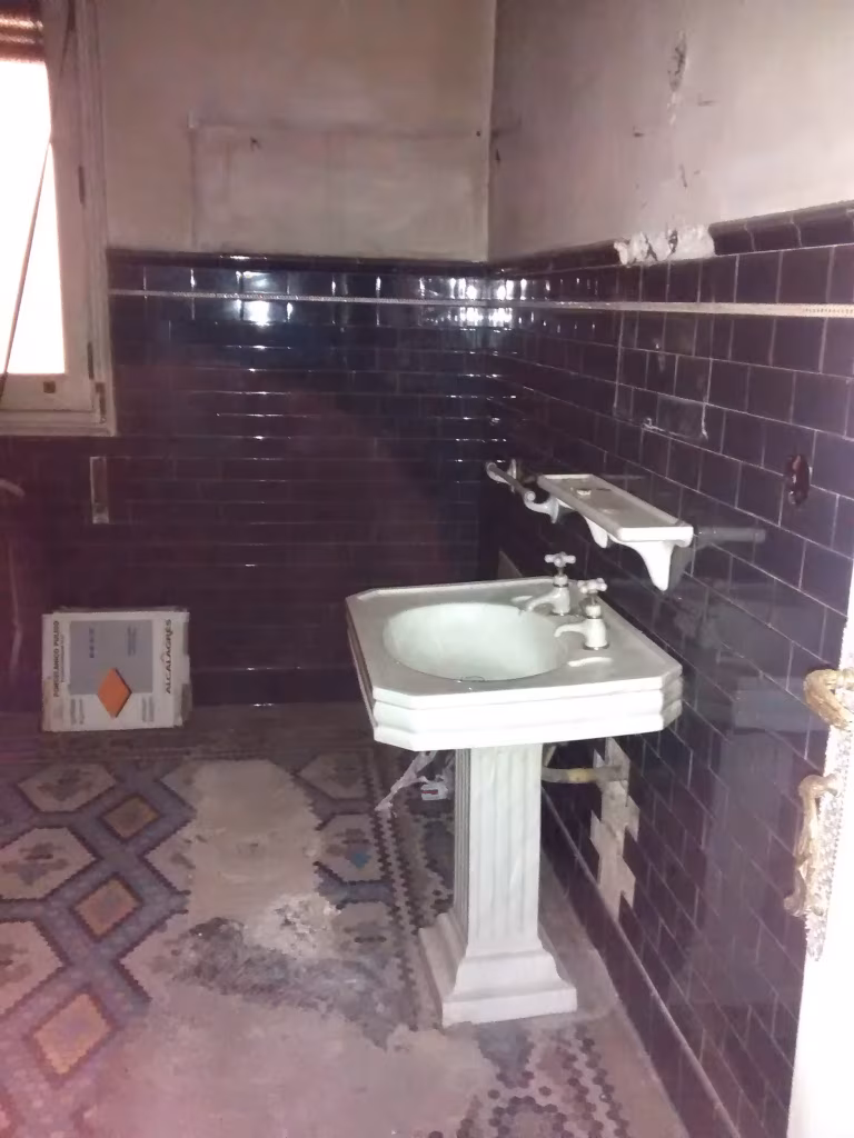 Antiguo baño de la vivienda antes de la obra, con lavabo de pie, azulejo oscuro y suelo hidráulico