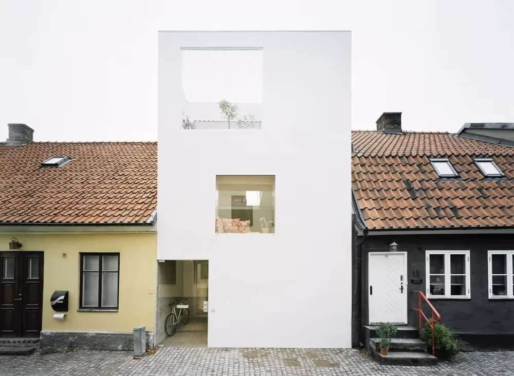 Townhouse de Elding Oscarson, fachada blanca con ventanas recortadas entre casas de tejas rojas en Landskrona