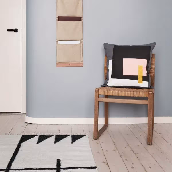 Silla de madera con cojín geométrico, organizador de tela colgado y alfombra de picos negros de Ferm Living