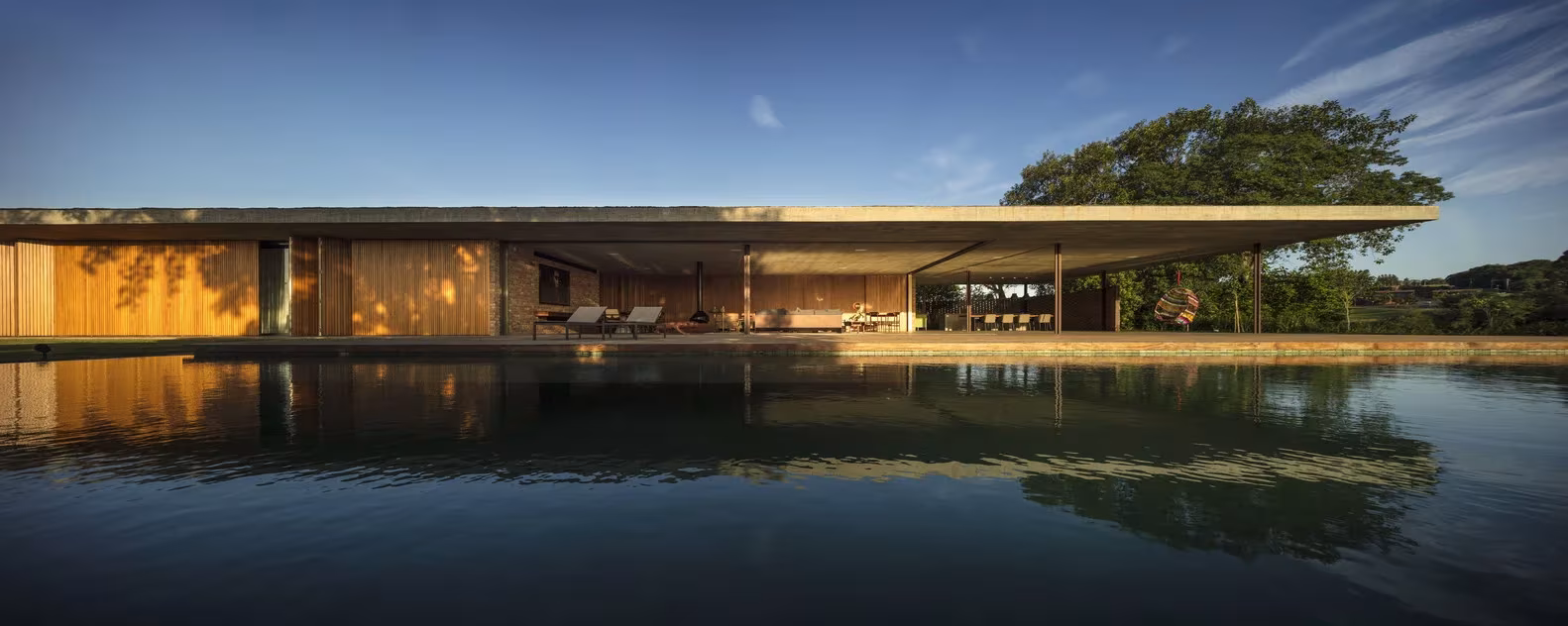 Casa plana de MK27 con losa de hormigón en voladizo reflejada en una lámina de agua al atardecer, Porto Feliz