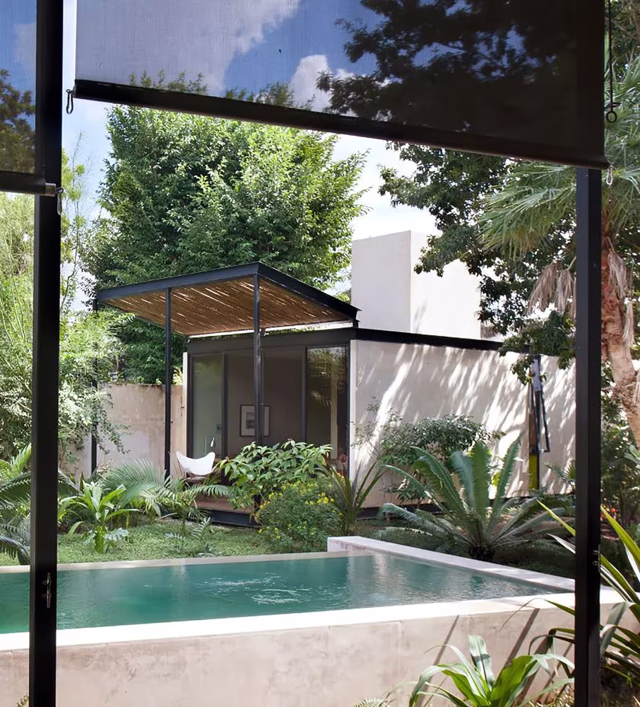 Piscina rectangular de la Casa Itzimná frente a un pabellón blanco con pérgola de bambú entre árboles