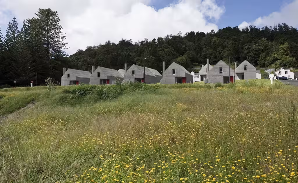 Hilera de casas de hormigón de Souto de Moura en Sete Cidades vistas desde un prado con flores