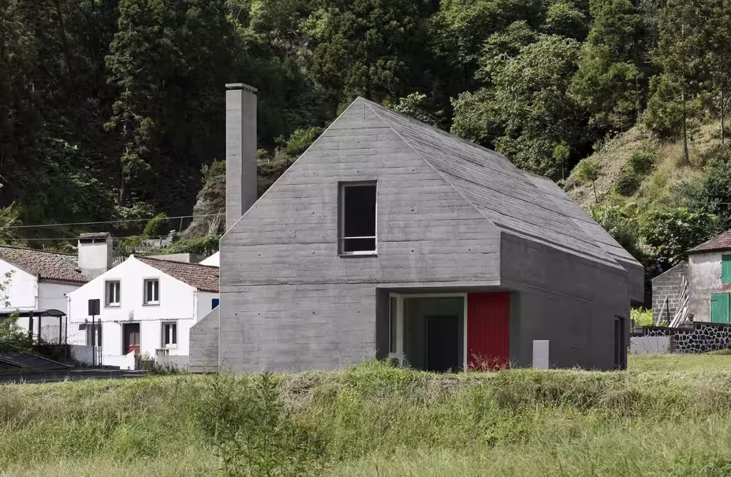 Casa de hormigón de cubierta a dos aguas y puerta roja en Sete Cidades junto a casas blancas tradicionales