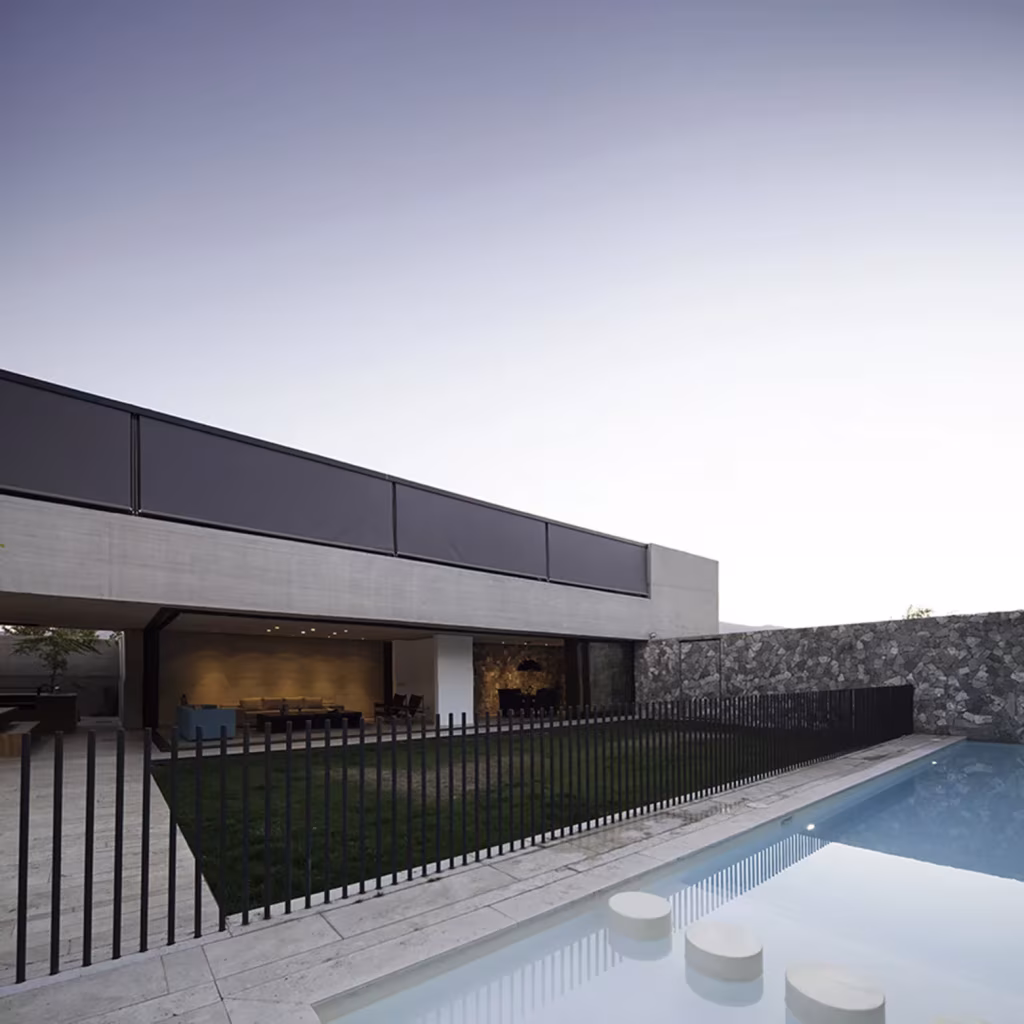 Piscina con escalones circulares junto a la Casa SH, barandilla negra, césped y volumen de hormigón en voladizo
