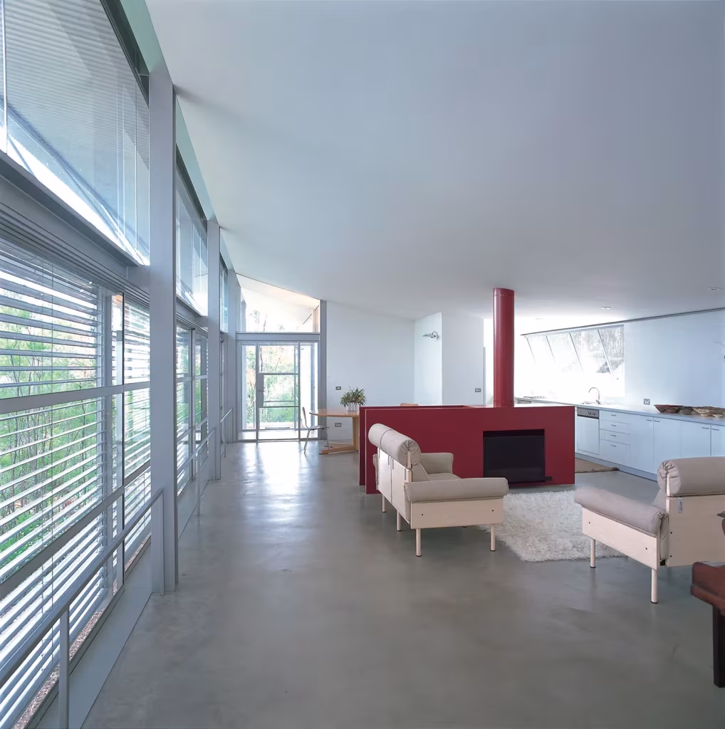 Interior de la casa Simpson-Lee de Glenn Murcutt con suelo de hormigón, chimenea roja y lamas en los ventanales