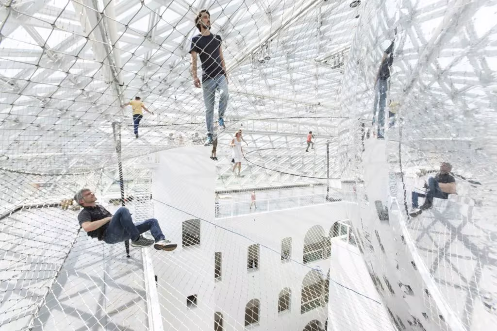 Visitantes caminando y tumbados sobre la red de acero suspendida de la instalación In Orbit de Tomás Saraceno