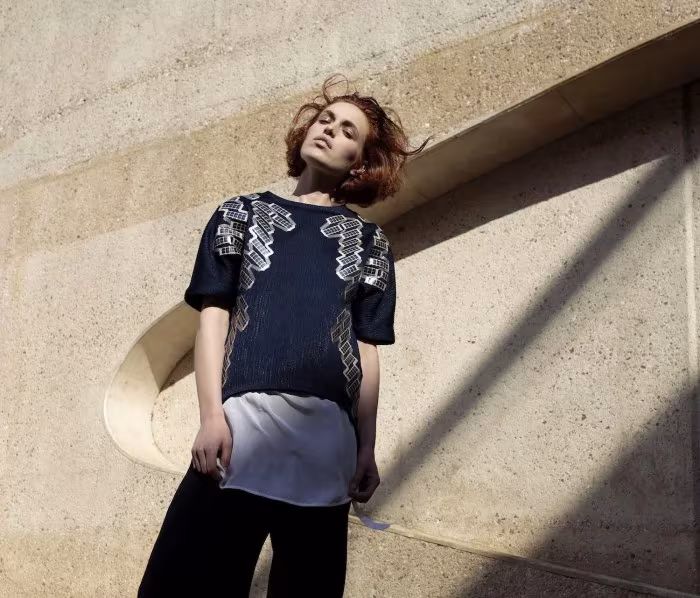 Modelo con prenda reflectante de Pauline van Dongen apoyada en un muro de hormigón al sol