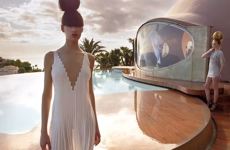Modelo con vestido blanco plisado junto a la piscina del Palais Bulles con el mar al fondo