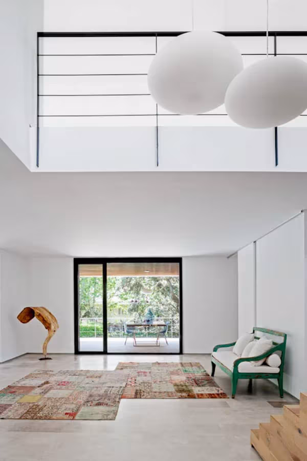 Salón de doble altura en La Moraleja con interiorismo de BATAVIA, lámparas de globo blancas, alfombra patchwork y banco verde