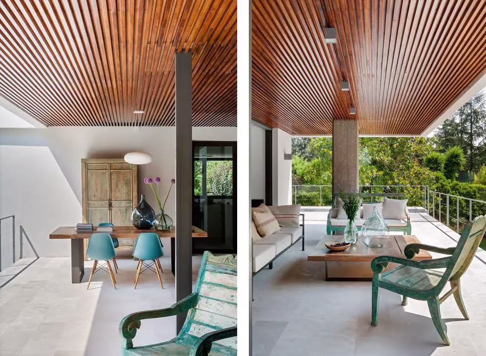 Comedor y terraza cubierta con techo de lamas de madera, sillas turquesa y sofá blanco abiertos al jardín en La Moraleja