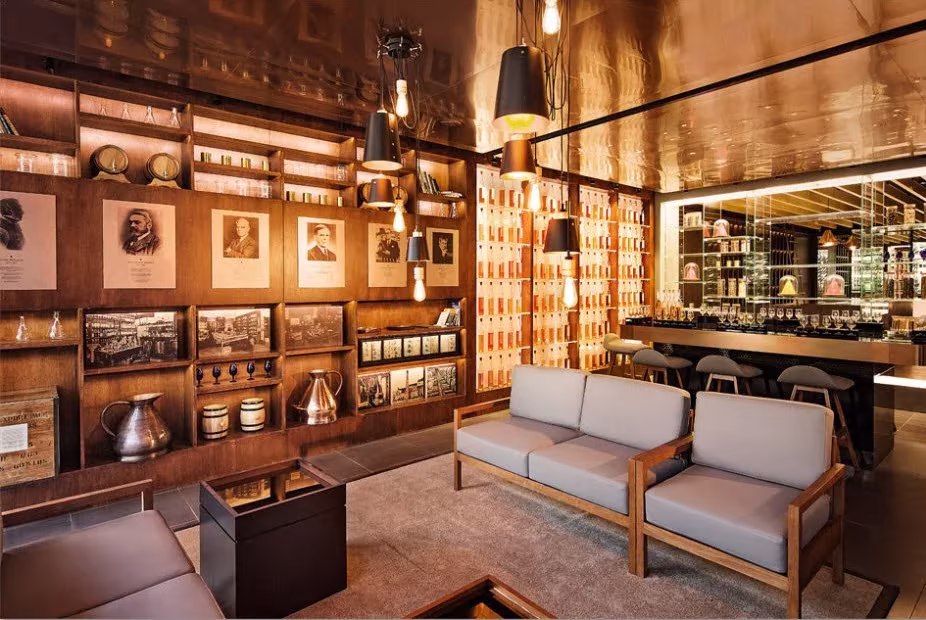 Biblioteca de whisky con estanterías de madera, sofás grises y lámparas negras en la Johnnie Walker House de Love