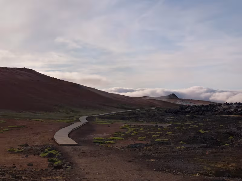 Camino sinuoso entre campos de lava oscura y colinas con nubes bajas al atardecer en Islandia