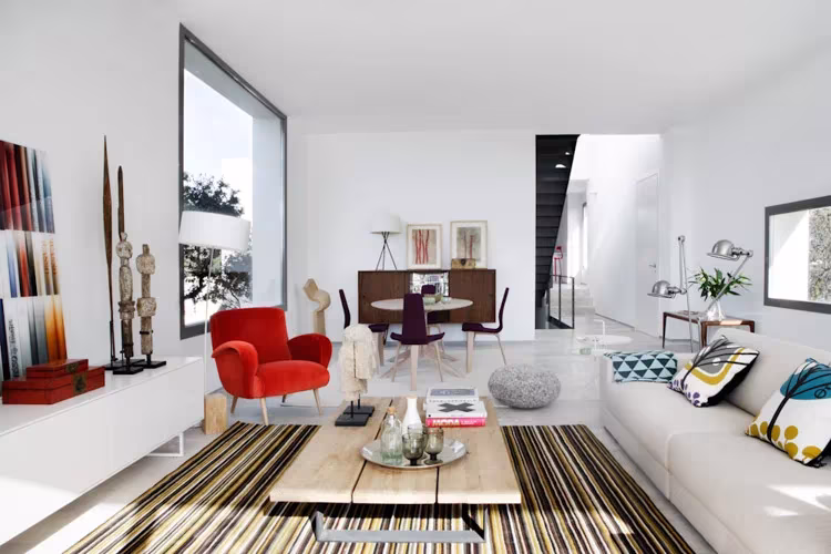 Salón amplio de Montealegría con alfombra de rayas, mesa baja de madera, sofá blanco y tallas de madera
