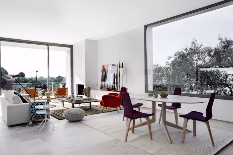 Salón y comedor diáfanos de Montealegría con ventanal de esquina, sofá blanco y sillas moradas