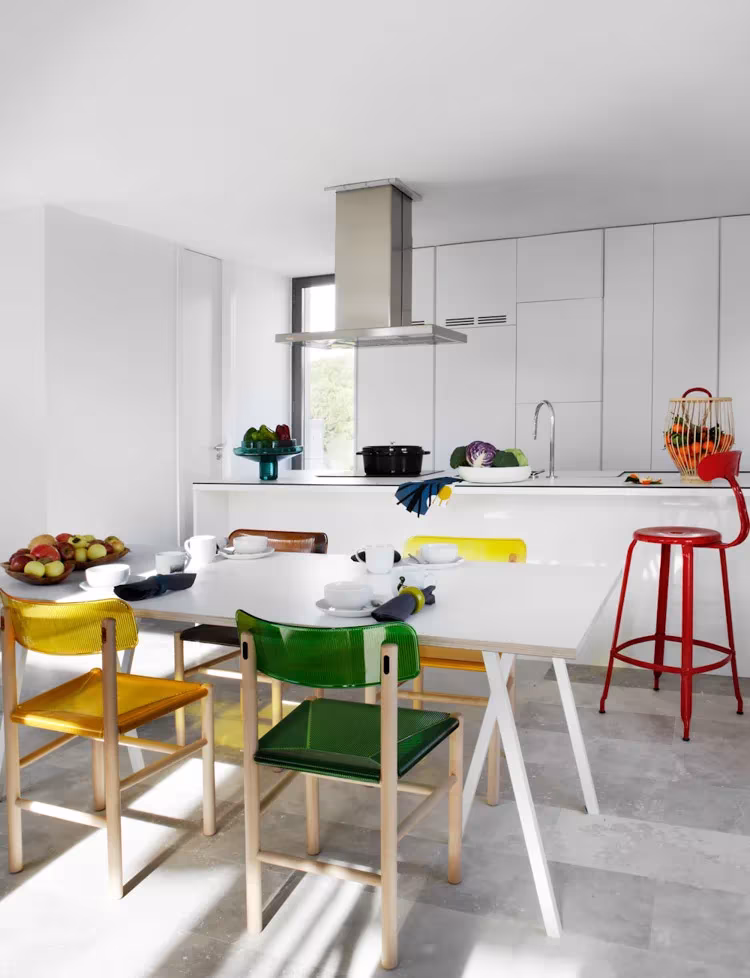 Cocina blanca de Montealegría con isla, campana de acero y sillas de colores alrededor de la mesa