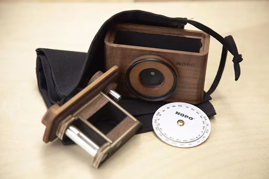 Cámara Nopo de nogal con su bolsa de tela negra, el carro de película y un disco calculador de exposición